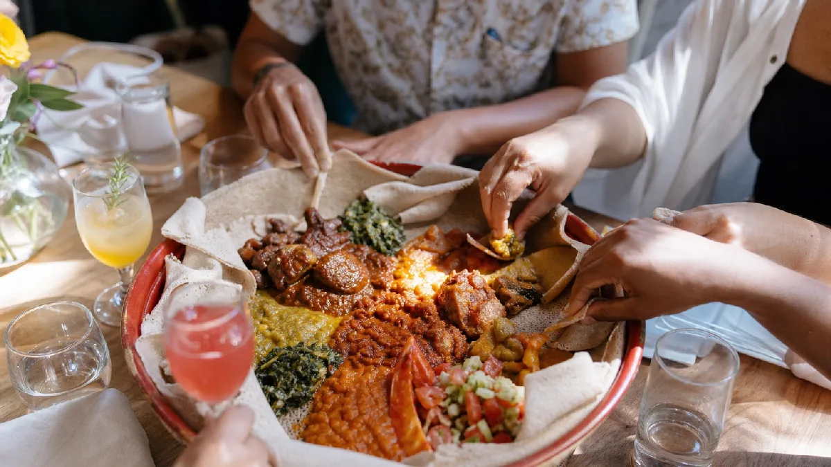 Friends sharing a traditional Ethiopian platter with injera and various stews at a cozy dining table.