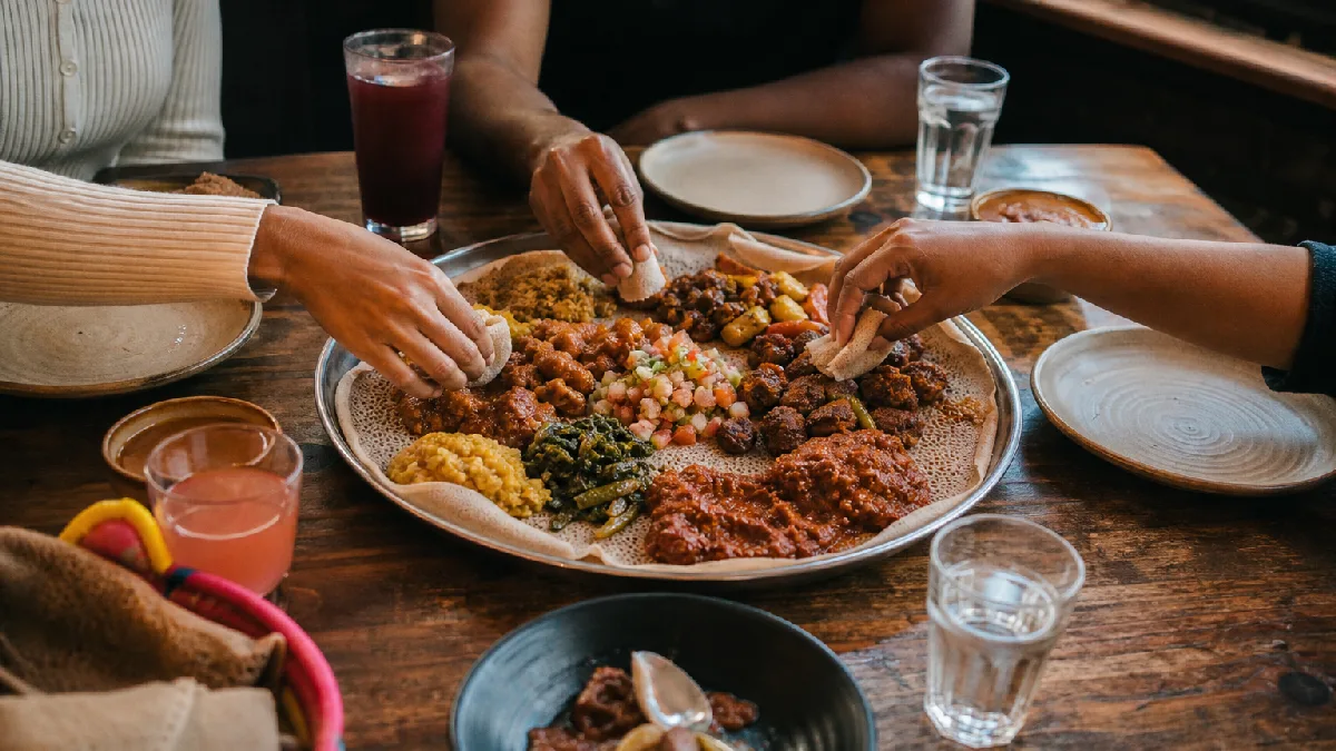 Communal injera platter with stews and vegetables shared by diners in a cozy restaurant setting.