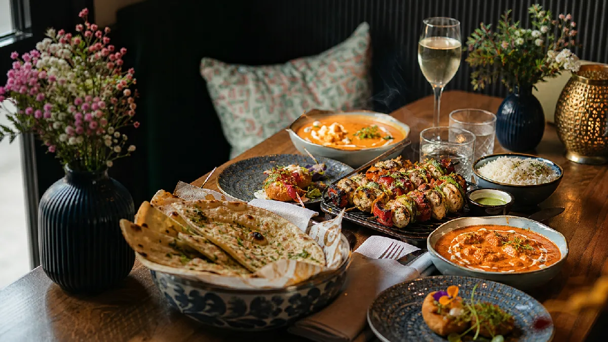 Table set with North Indian breads, grilled skewers, curries, and rice in a warmly lit restaurant dining room.