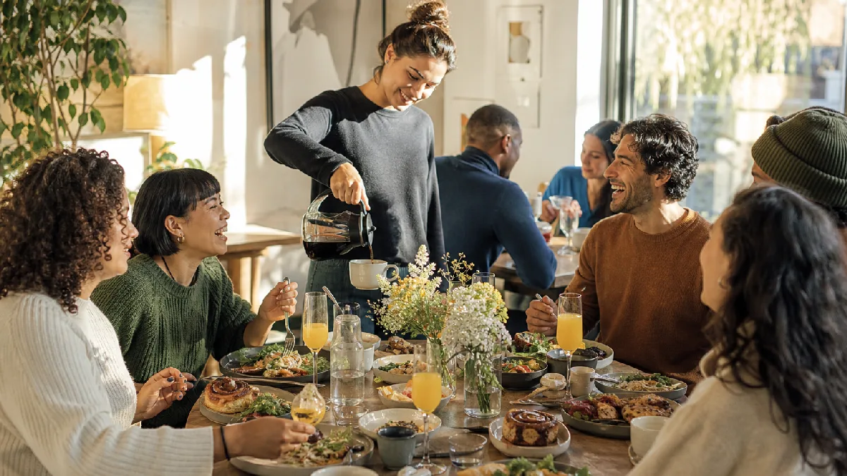 Friends enjoying a sunny weekend brunch with plant-based dishes and coffee in a cozy, contemporary café dining room.