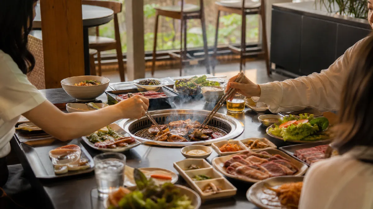 Friends gathered around a Korean barbecue grill at a modern restaurant enjoying grilled meats and side dishes.